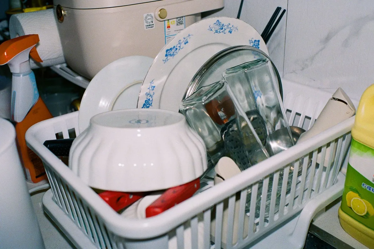 Clean plates and glasses drying in a dish rack with cleaning supplies, highlighting the importance of proper dishwasher funct