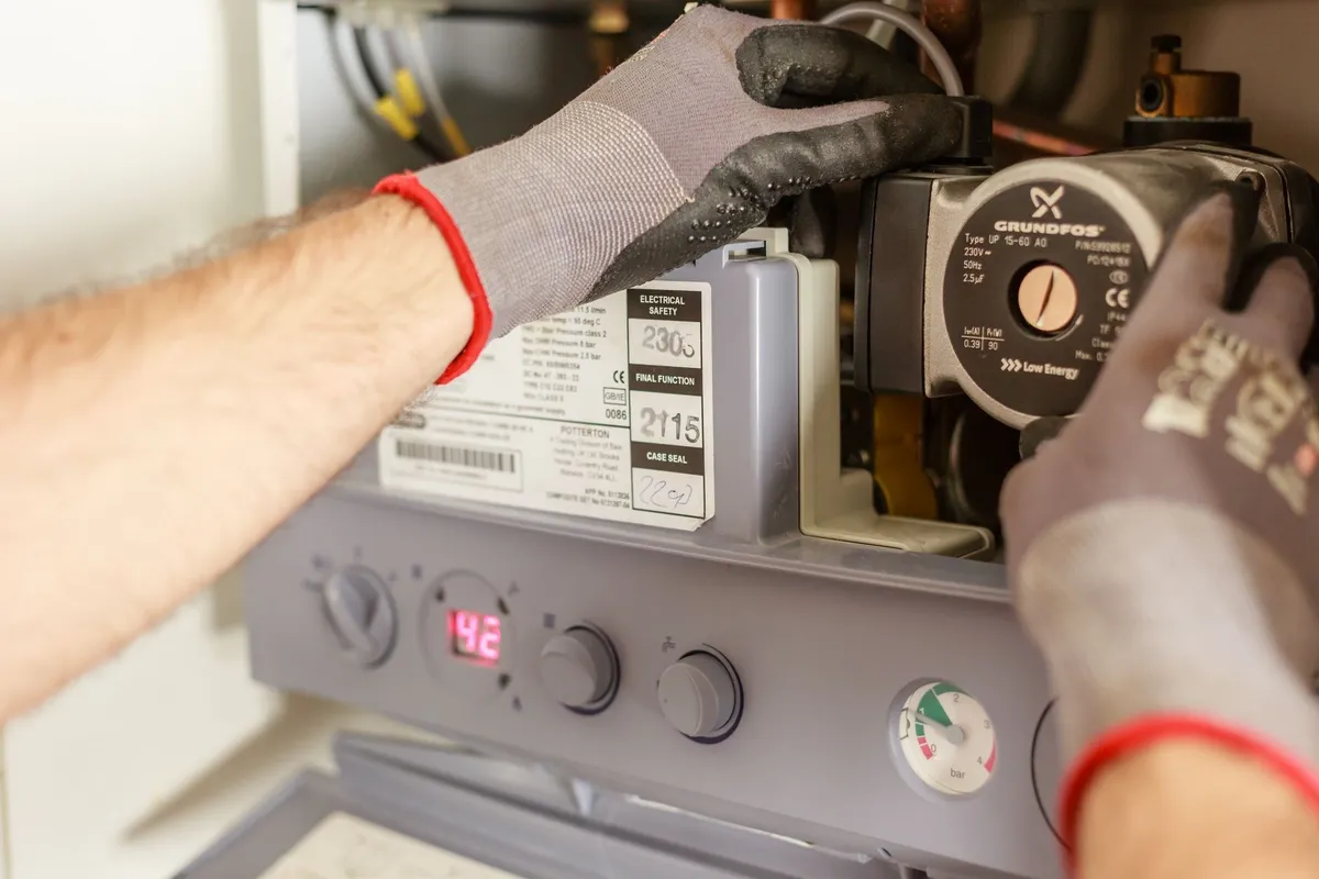 Hands carefully adjusting a boiler system, illustrating the importance of timely appliance maintenance.